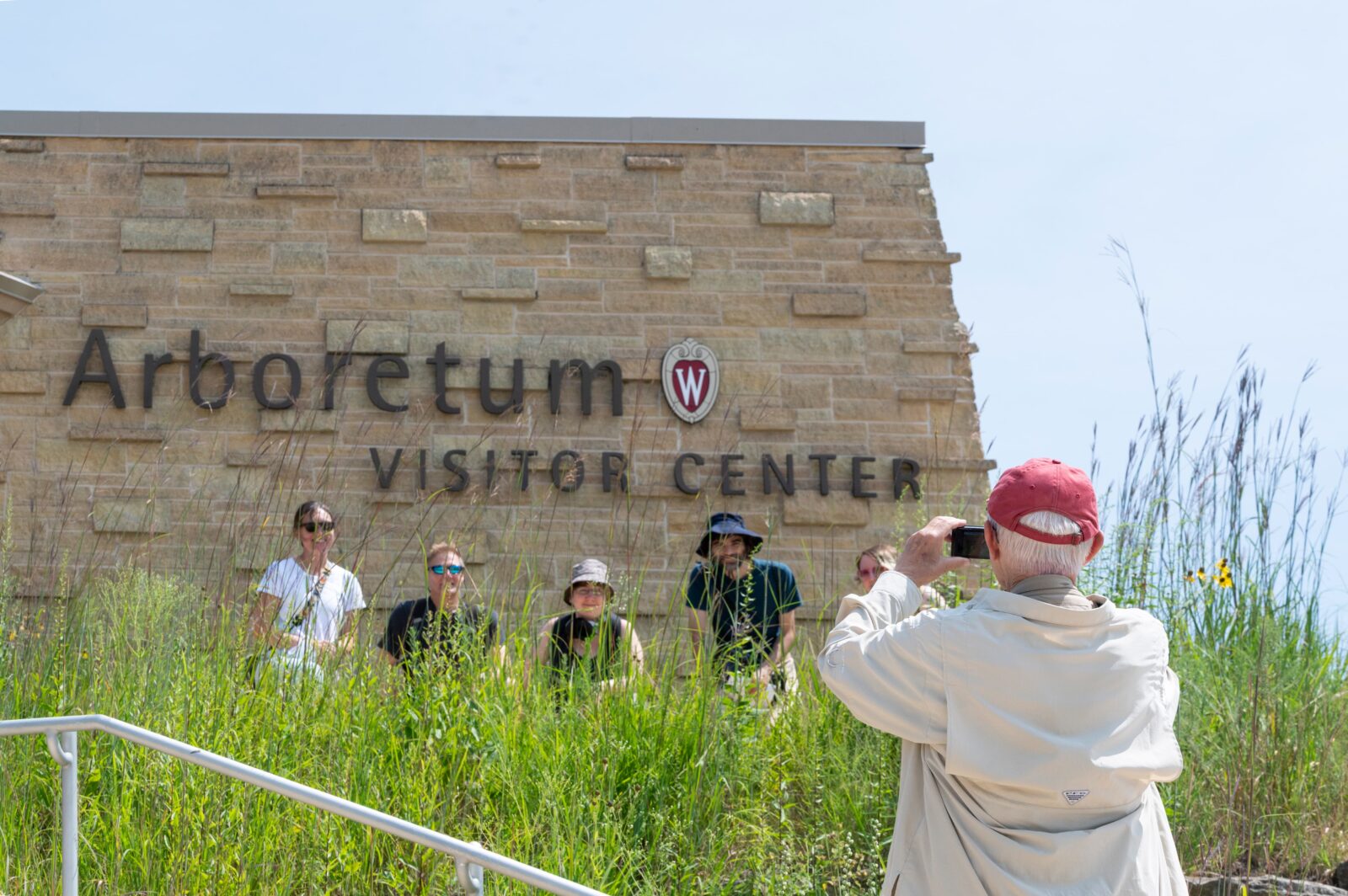 Chuck Henrikson (right) takes a photo of his birding troop before seeing off on an expedition during the McPherson Eye Research Institute’s Vision at the Arboretum event at the University of Wisconsin–Madison Arboretum on Aug. 8, 2026. The event was a family-friendly education event, educating people of all ages on bird vision, care, and daily life. (Photo by Jake Piper / UW–Madison)